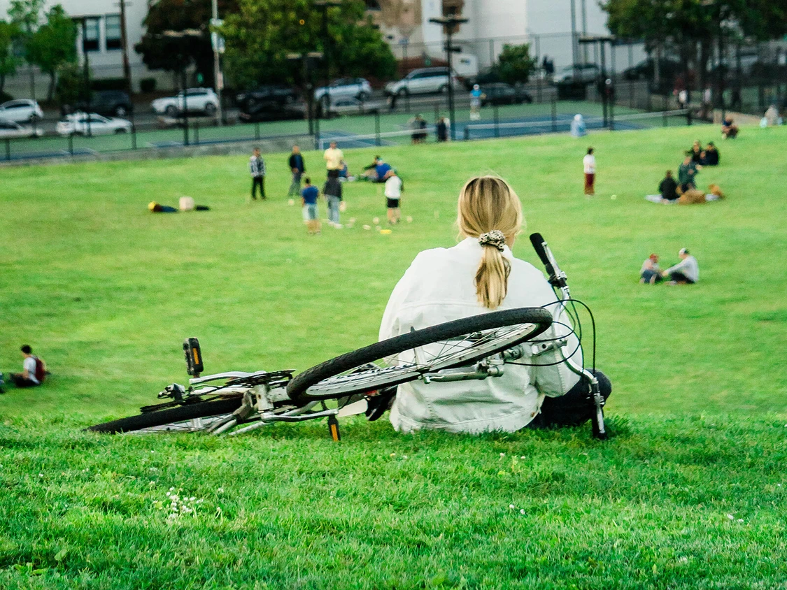 Frau sitzt mit einem fahrrad neben ihr auf einem h&uuml;gel